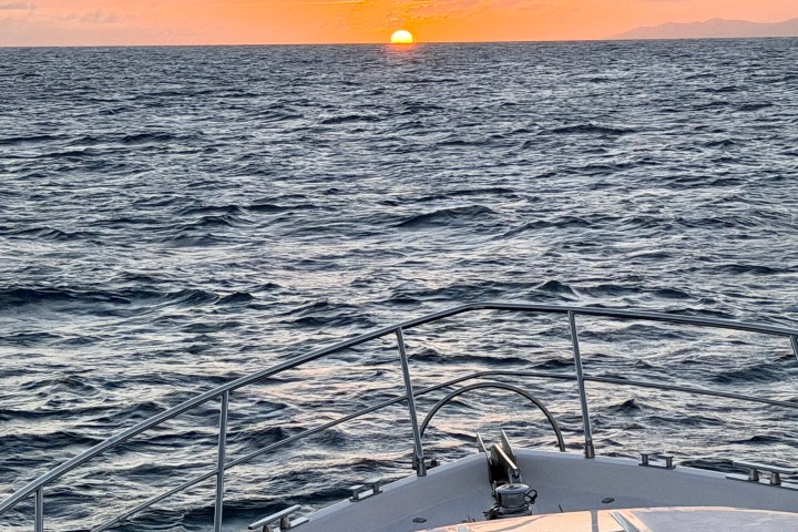 Boat on ocean with sunset on horizon and orange sky.