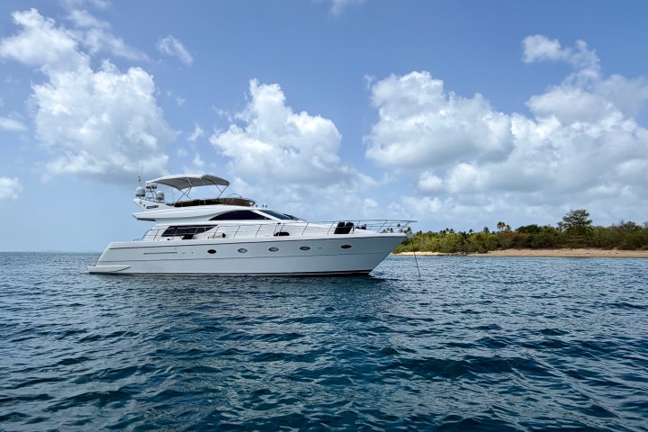 White yacht anchored near a coastline under a partly cloudy sky.