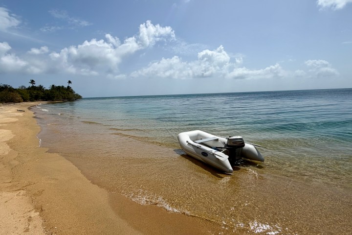 Inflatable boat on a sandy beach with calm sea and blue sky.