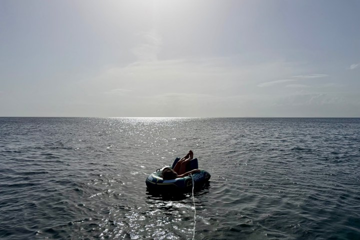 Person on floating raft in sunny ocean under clear sky.