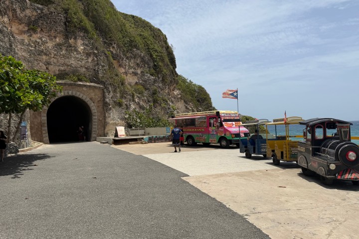 Tourist area with tunnel, colorful bus, and small train near cliffs and ocean.