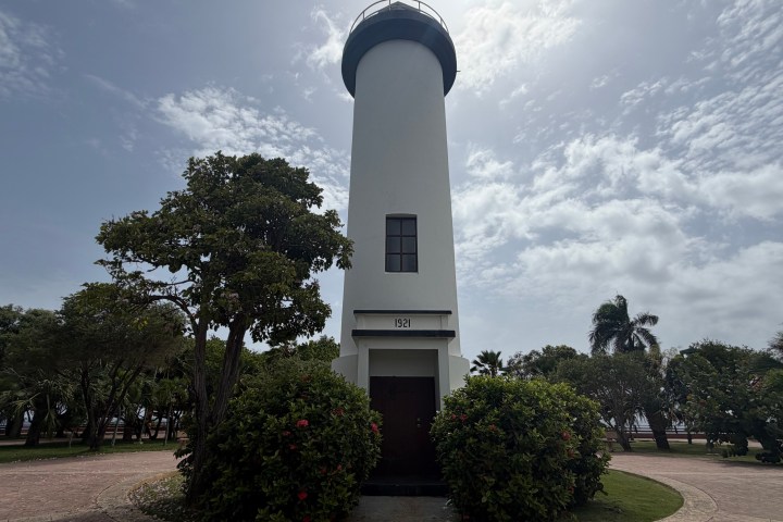 Tall white lighthouse surrounded by trees under a cloudy sky.